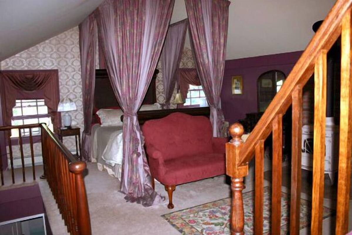Ein Schlafzimmer mit einem Himmelbett, einer Holztreppe und einem roten Sessel.