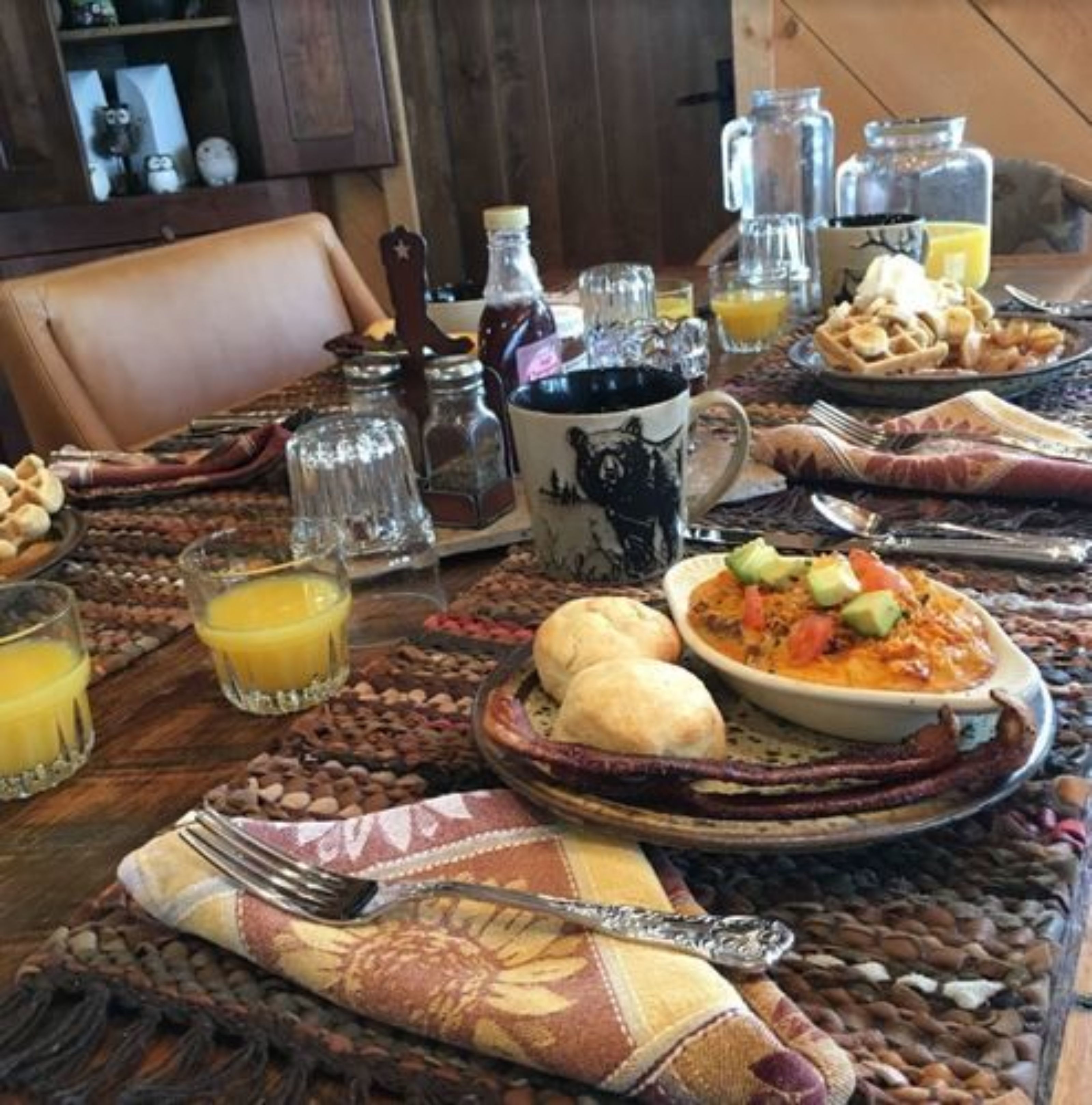 A dining table set with various dishes, including a bowl of soup, bread, and a plate of food. There are also glasses of orange juice and a pitcher of water.