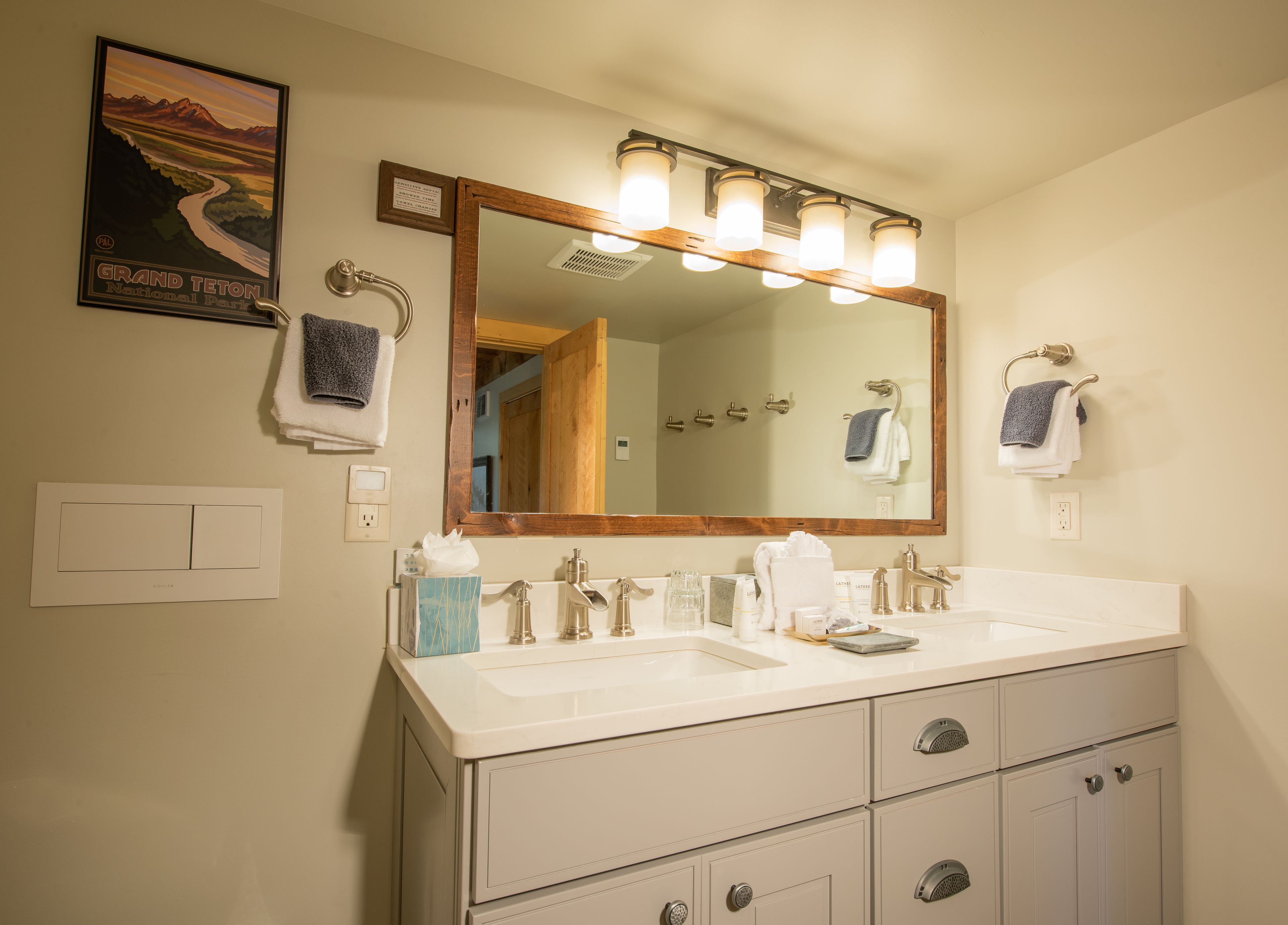A bathroom with a double sink, a large mirror, and a poster of Grand Teton National Park.