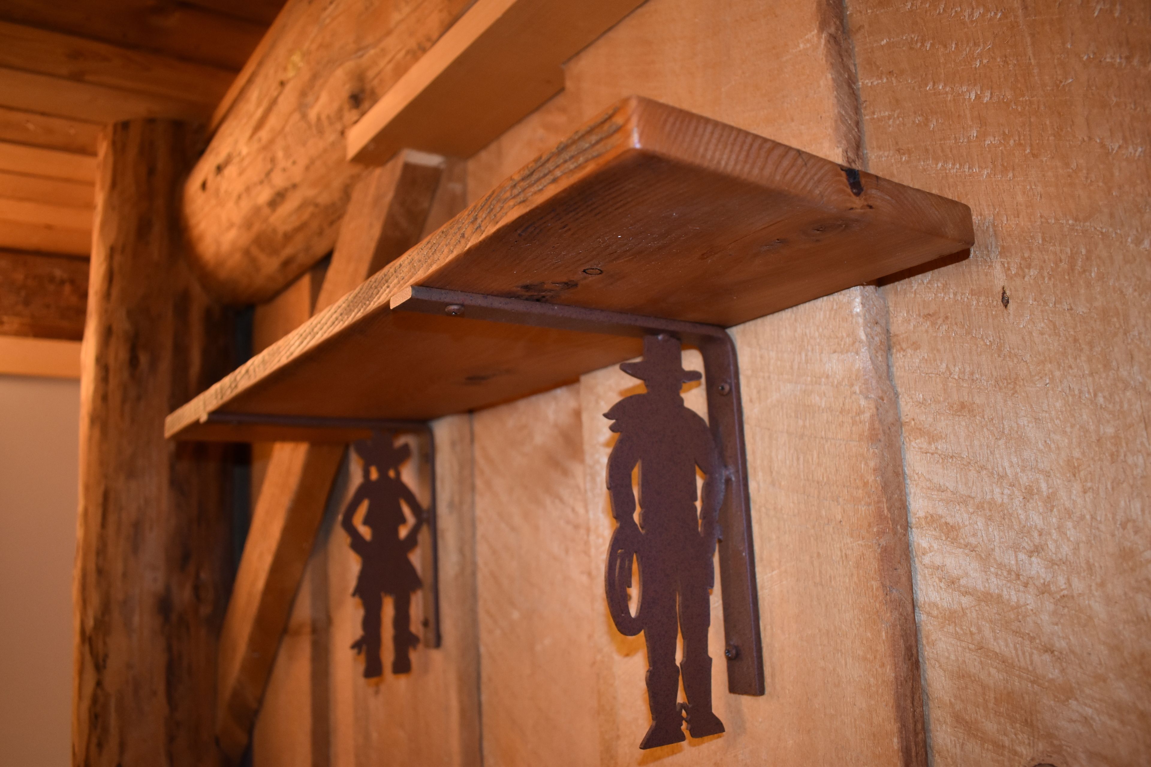 Un muro in legno rustico con staffe metalliche e le sagome di un cowboy e un bambino.