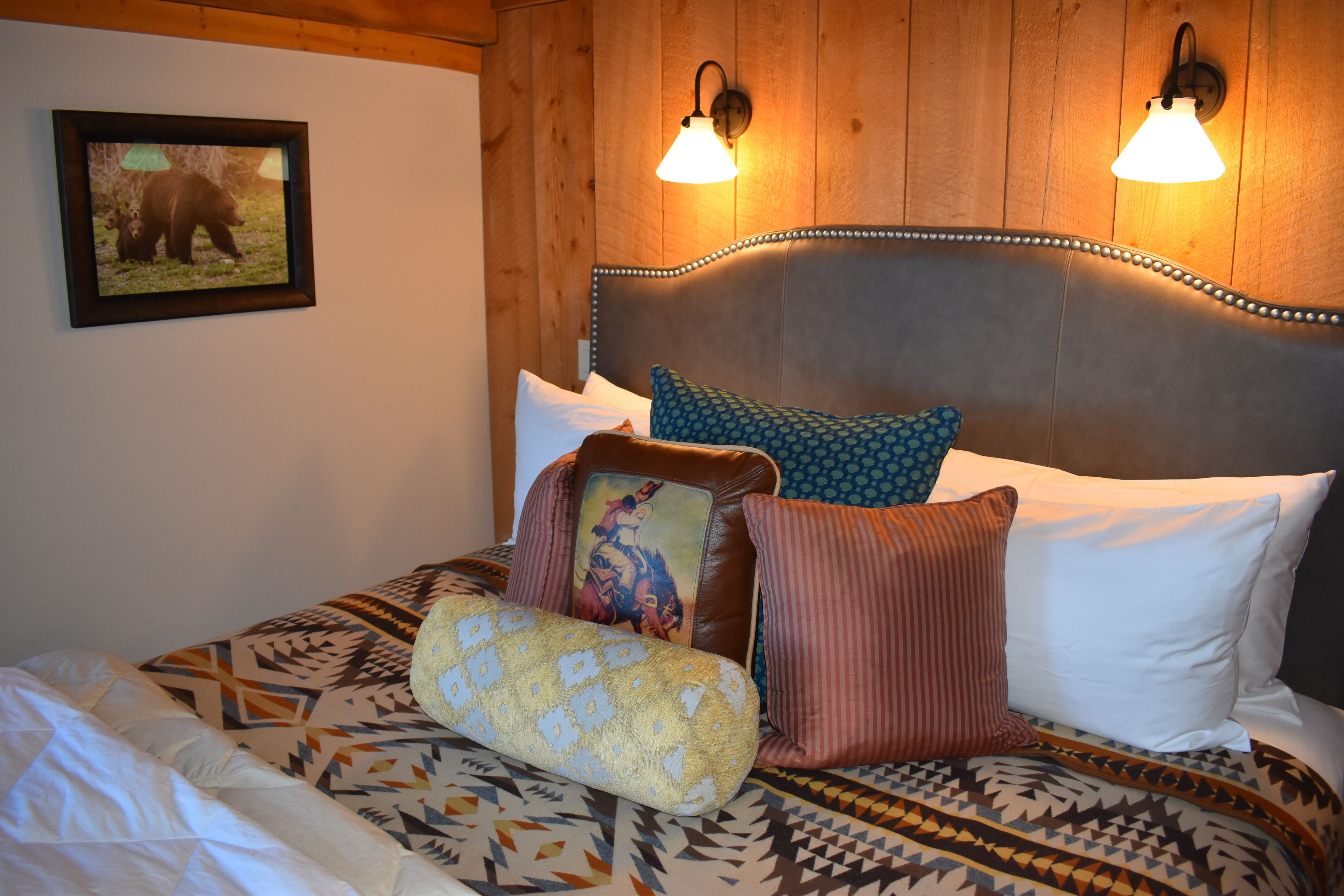 A bed with patterned bedding, a headboard with a decorative trim, and two wall-mounted lights.