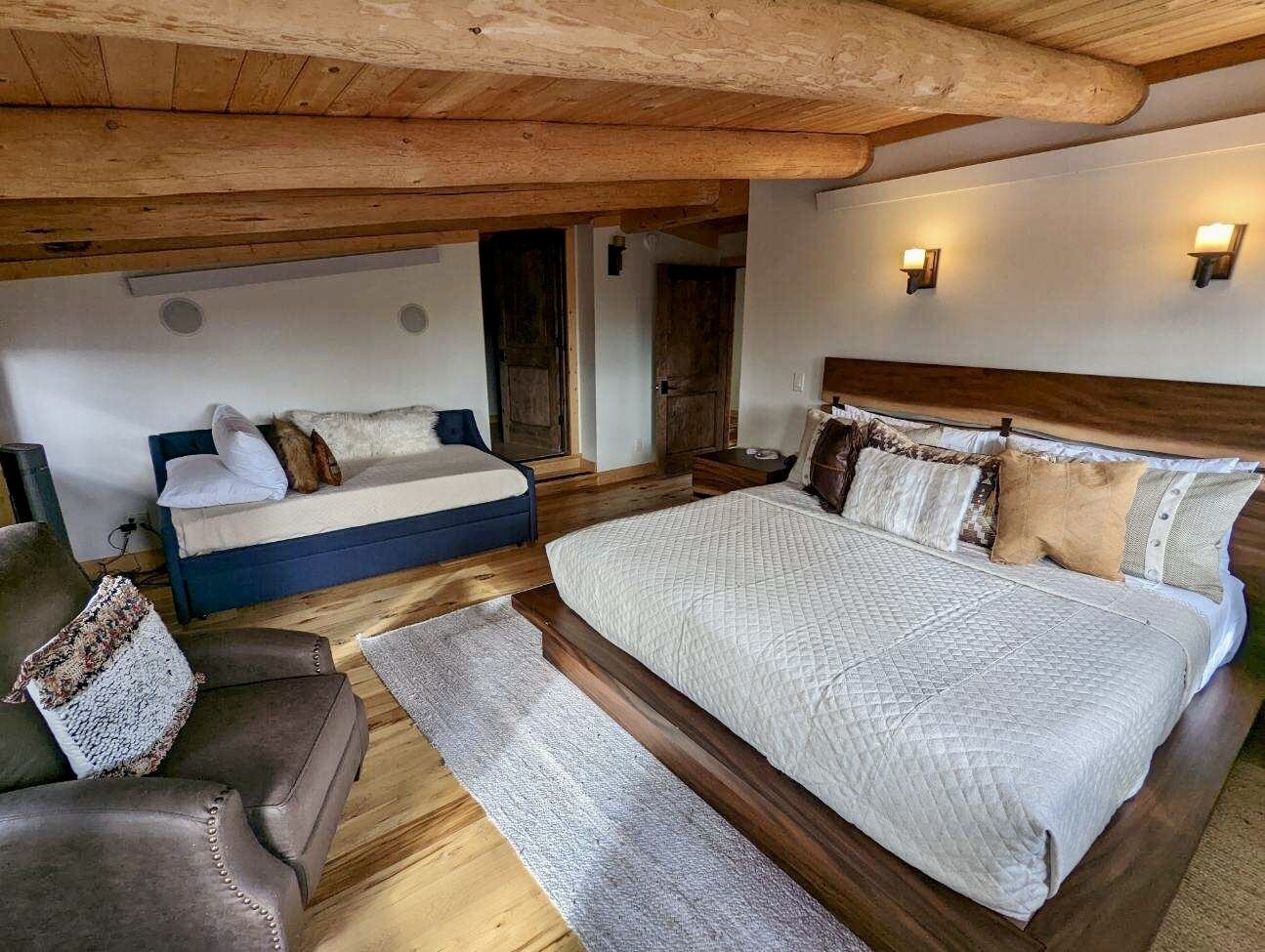 A bedroom with a large bed, a smaller sofa, and a wooden ceiling.