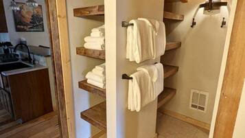 Bany compacte amb prestatges de fusta per als draps, zona de dutxa oberta i cuina petita amb un rentapeus i llums penjants.