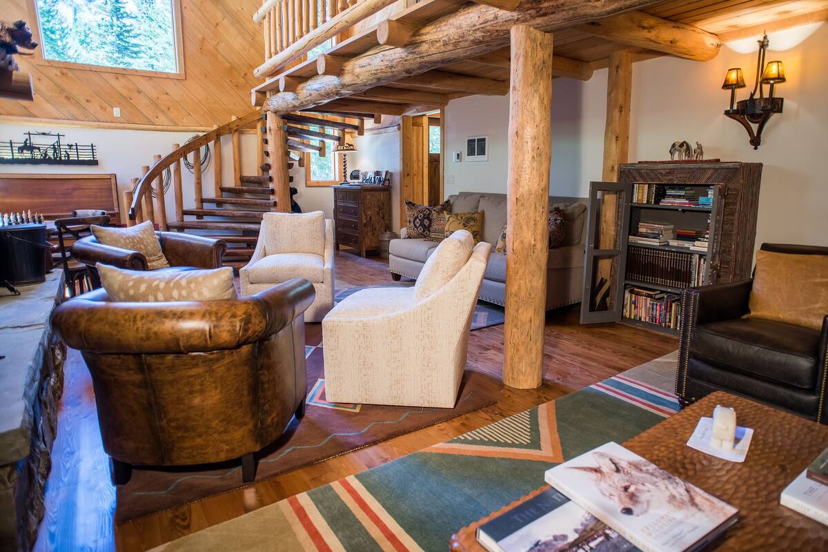 Amplia sala de estar con escalera de madera, sofás de cuero y tela, una estantería y una chimenea.