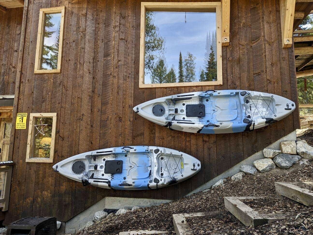 Two kayaks mounted on a wooden wall with a caution sign and a window reflecting trees.