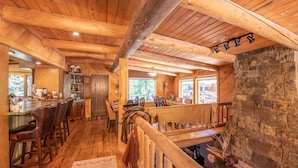 A rustic interior with wooden beams, a stone fireplace, a bar area, and a dining space.
