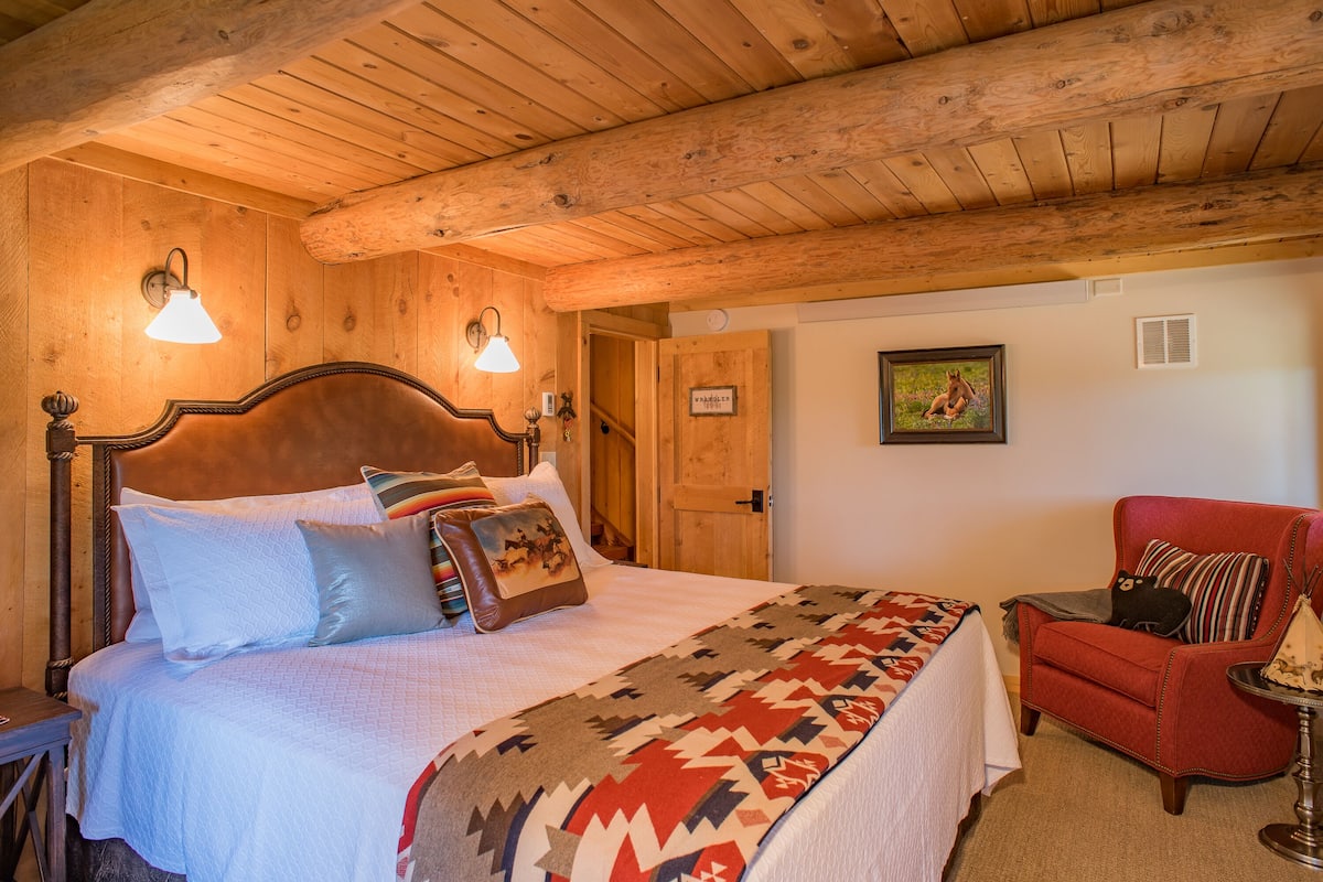 Un dormitorio de cabaña de madera con una cama, un sillón rojo y un cuadro en la pared.