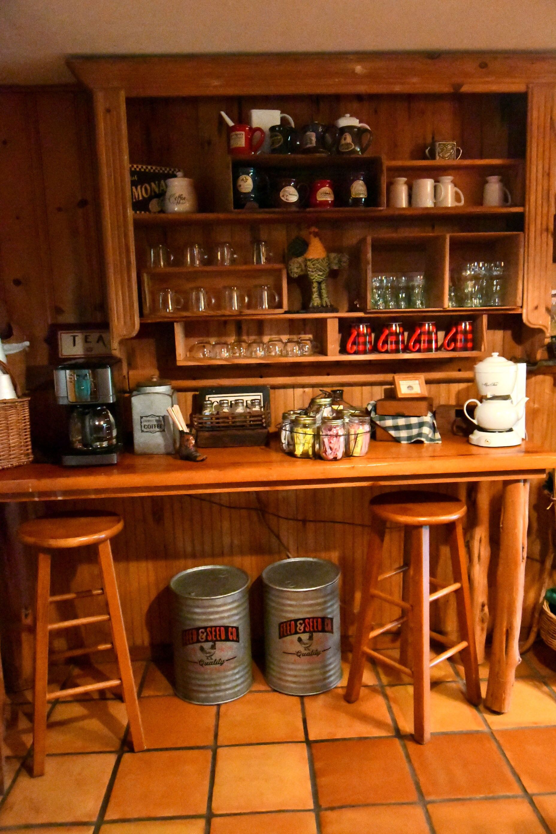 Una cocina con estantes de madera, una cafetera y dos taburetes.