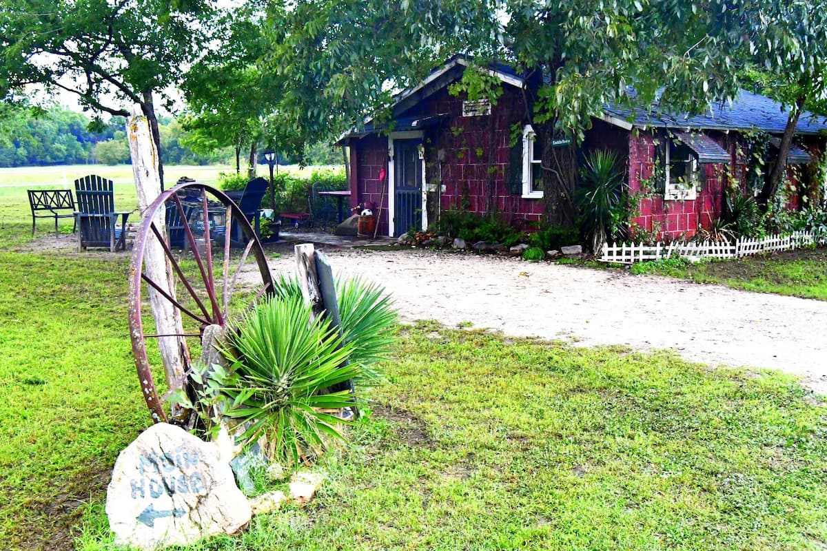 A rustic house with a white picket fence, a large tree, and a sign that reads "Old House."