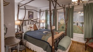 A bedroom with a four-poster bed, a wooden desk, a chair, and a view of a church through the window. - Country Woods Inn (Glen Rose)