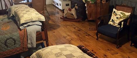 A cozy attic bedroom with wooden floors, a bed with a quilt, a rocking chair, and a dresser with stuffed animals.
