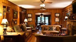 A cozy living room with wooden paneling, leather sofas, and a dining area with a table and chairs. - Country Woods Inn (Glen Rose)