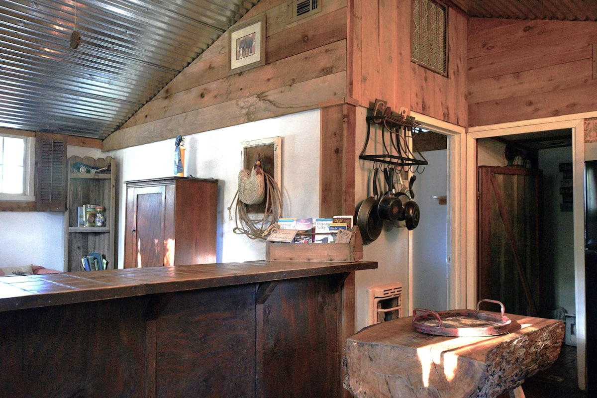 A rustic kitchen with wooden walls, a wooden counter, and hanging pots.
