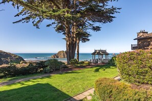 A garden with a gazebo, a large tree, and a view of the ocean.