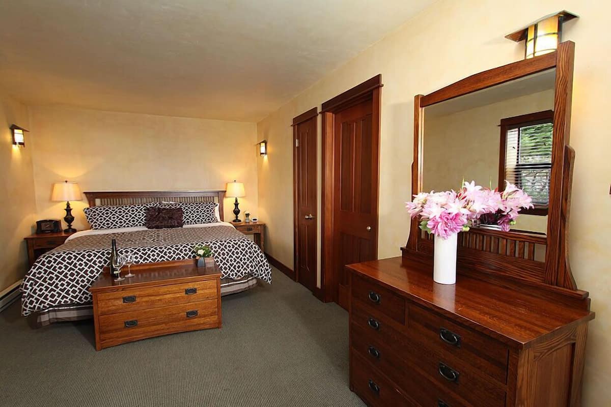 A bedroom with a bed, bedside tables, a dresser, a mirror, and a vase with flowers.