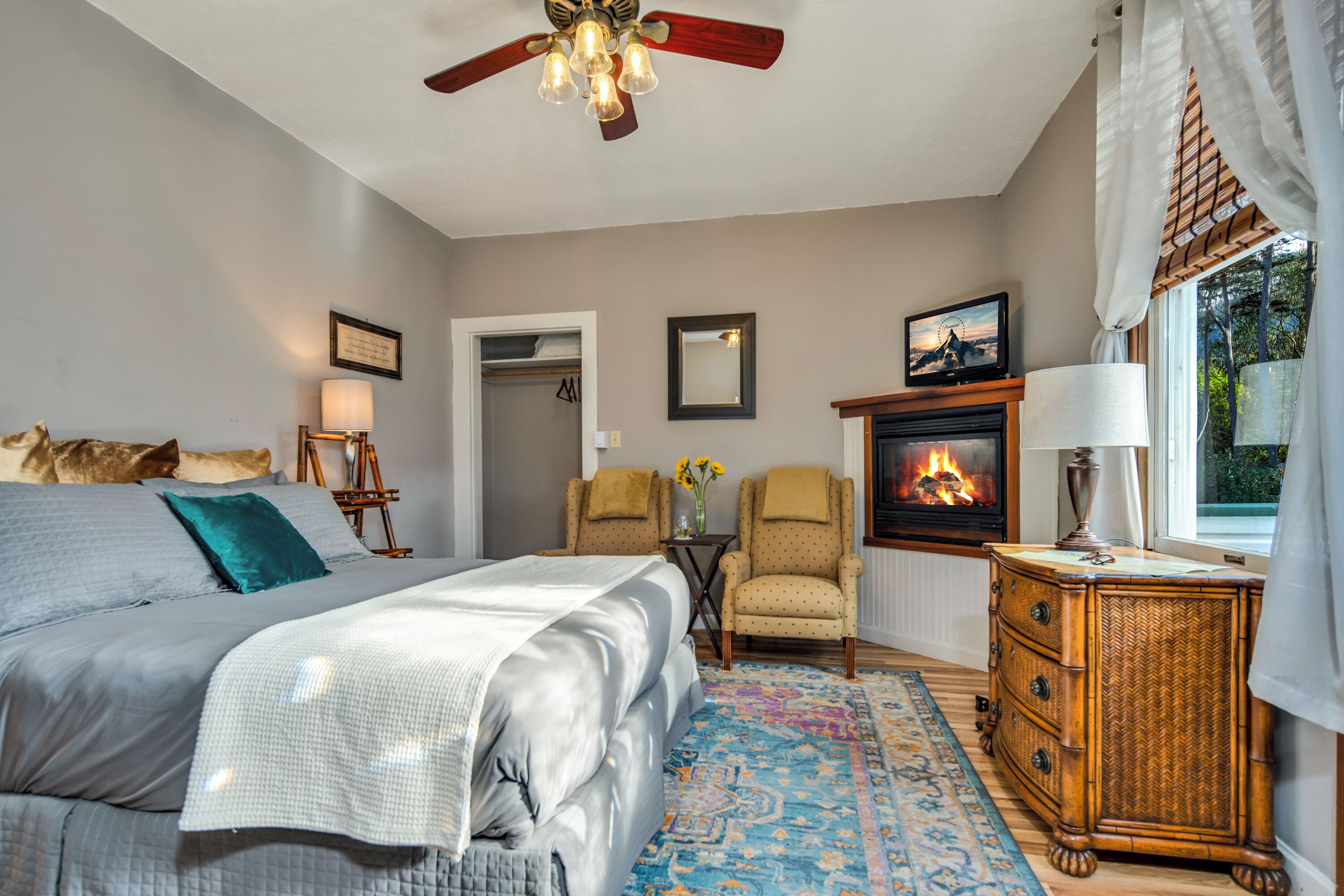 A bedroom with a bed, a chair, a dresser, a fireplace, and a ceiling fan.