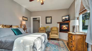 A bedroom with a bed, a chair, a dresser, a fireplace, and a ceiling fan.