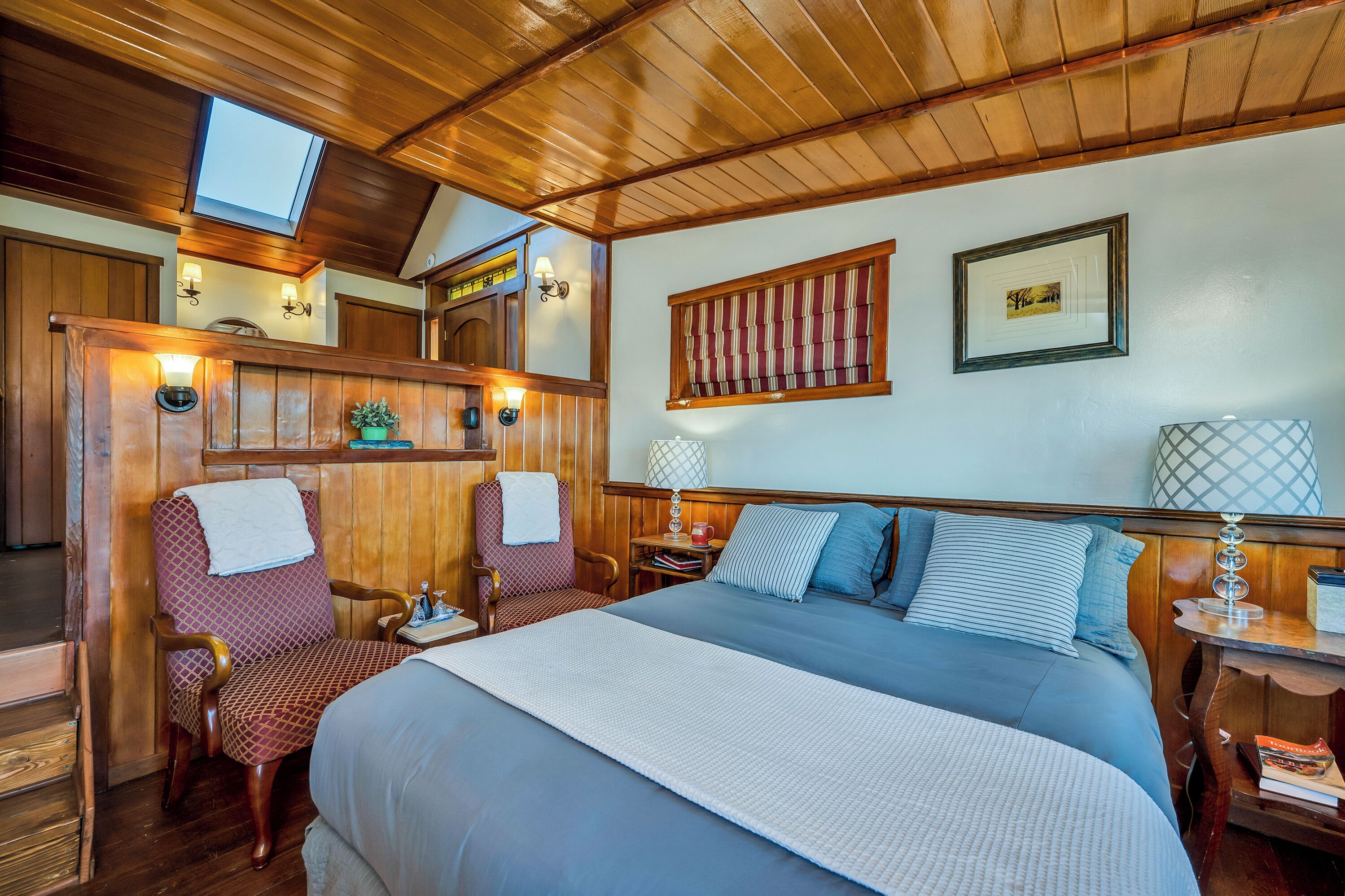 A cozy bedroom with a large bed, two chairs, a nightstand, and a skylight.