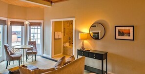 A cozy room with a sofa, a small table, and chairs. There is a bathroom with a shower and a mirror.