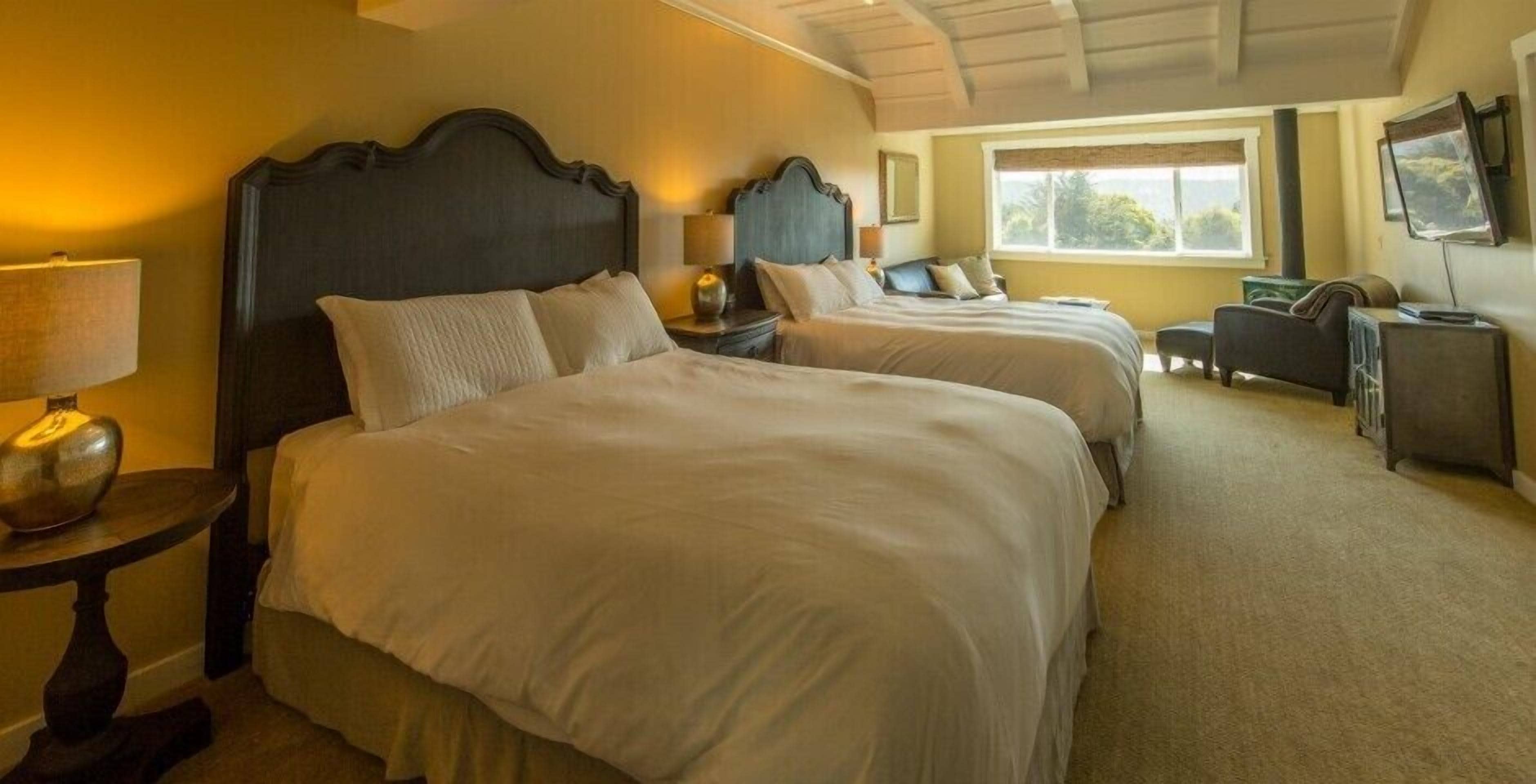 A hotel room with two beds, a sofa, a TV, and a window with a view.