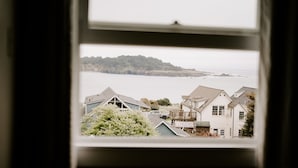 A view through a window of a coastal residential area with houses and a body of water in the background. - MacCallum House Inn (Mendocino)