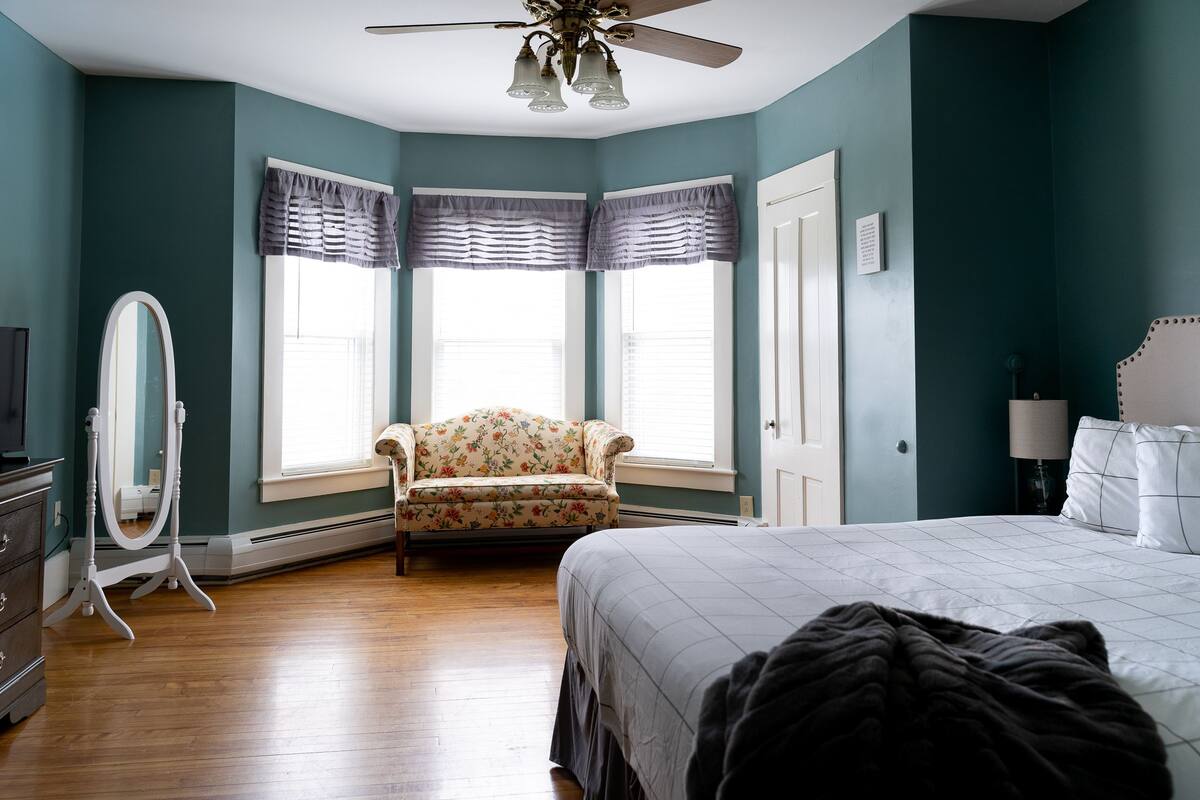 A bedroom with a bed, a chair, a dresser, and a mirror.