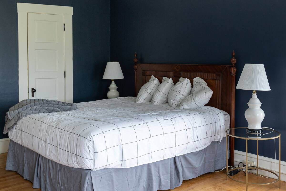 A bedroom with a bed, two bedside lamps, a wooden headboard, and a white door.