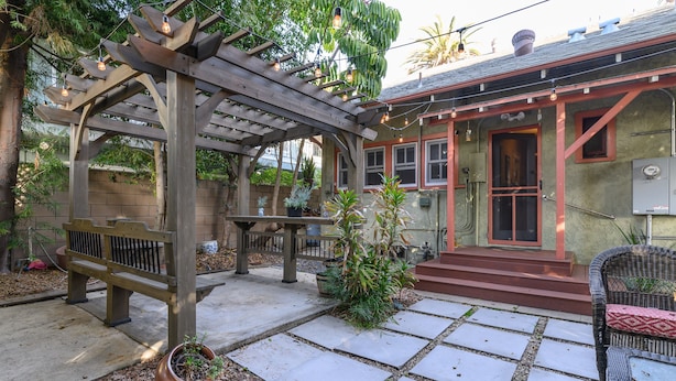 A covered patio area with a pergola, seating, and potted plants.