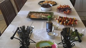 A dining table set with various food items, including a plate of croissants, a bowl of grapes, and skewers of vegetables.