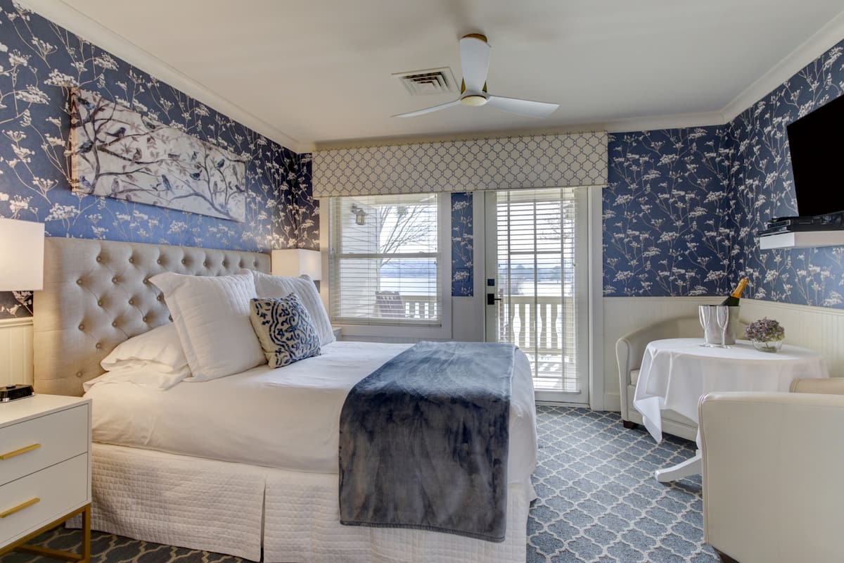 A bedroom with a large bed, a ceiling fan, a nightstand, a bedside table, a chair, and a television.