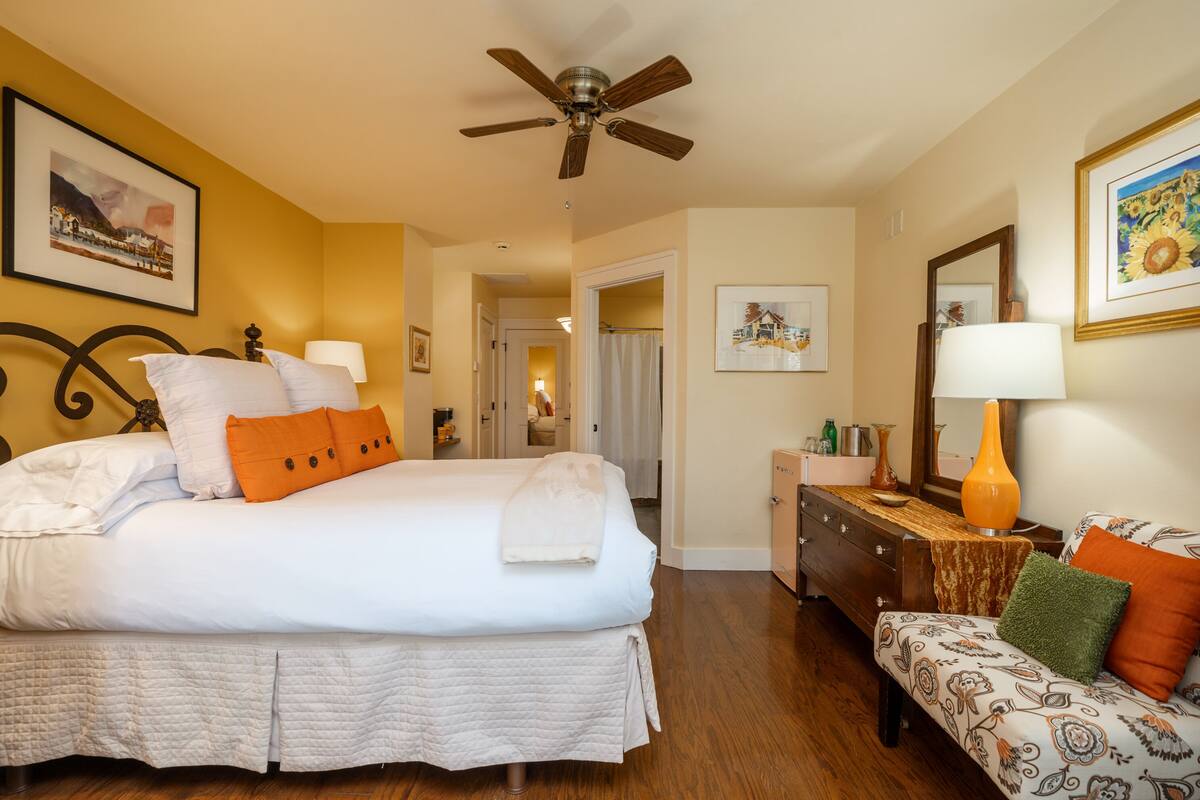 A hotel room with a bed, bedside table, lamp, and a bench with cushions.