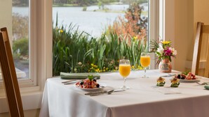 Une table à manger dressée avec un repas, un verre de jus d’orange et un vase de fleurs.