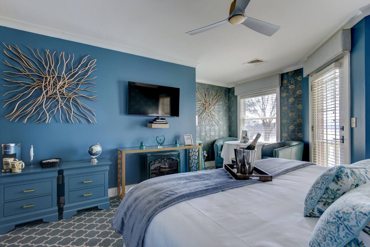 A bedroom with a bed, a desk, a television, and a ceiling fan.