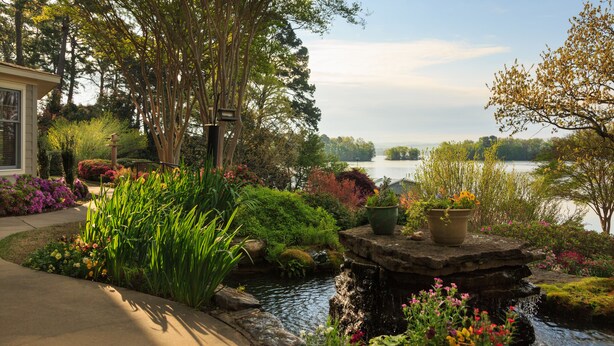 Un jardin aménagé avec un étang, différentes espèces de plantes et une vue sur un lac.