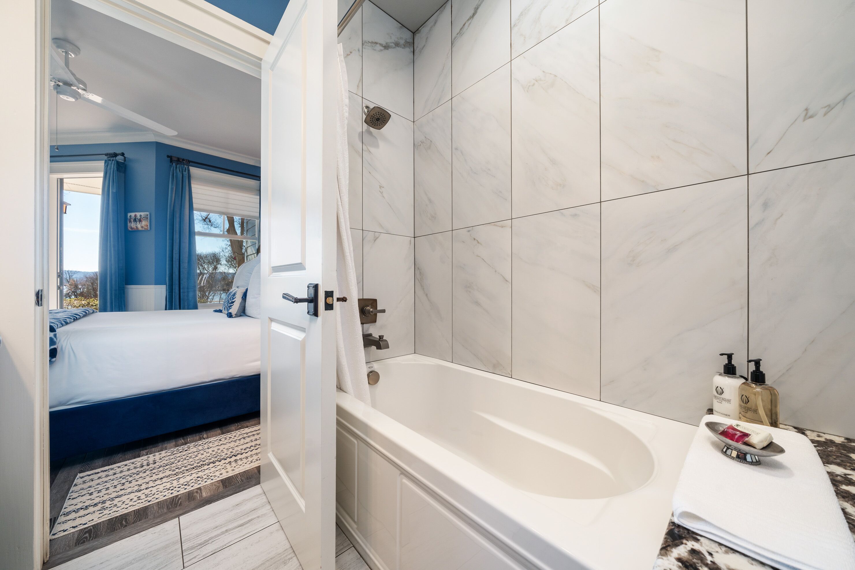Une salle de bain moderne avec une baignoire, des carreaux de marbre blanc et une pomme de douche visible.