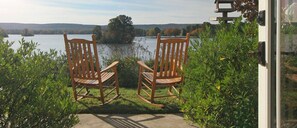 Two rocking chairs facing a lake with a view of hills in the distance.