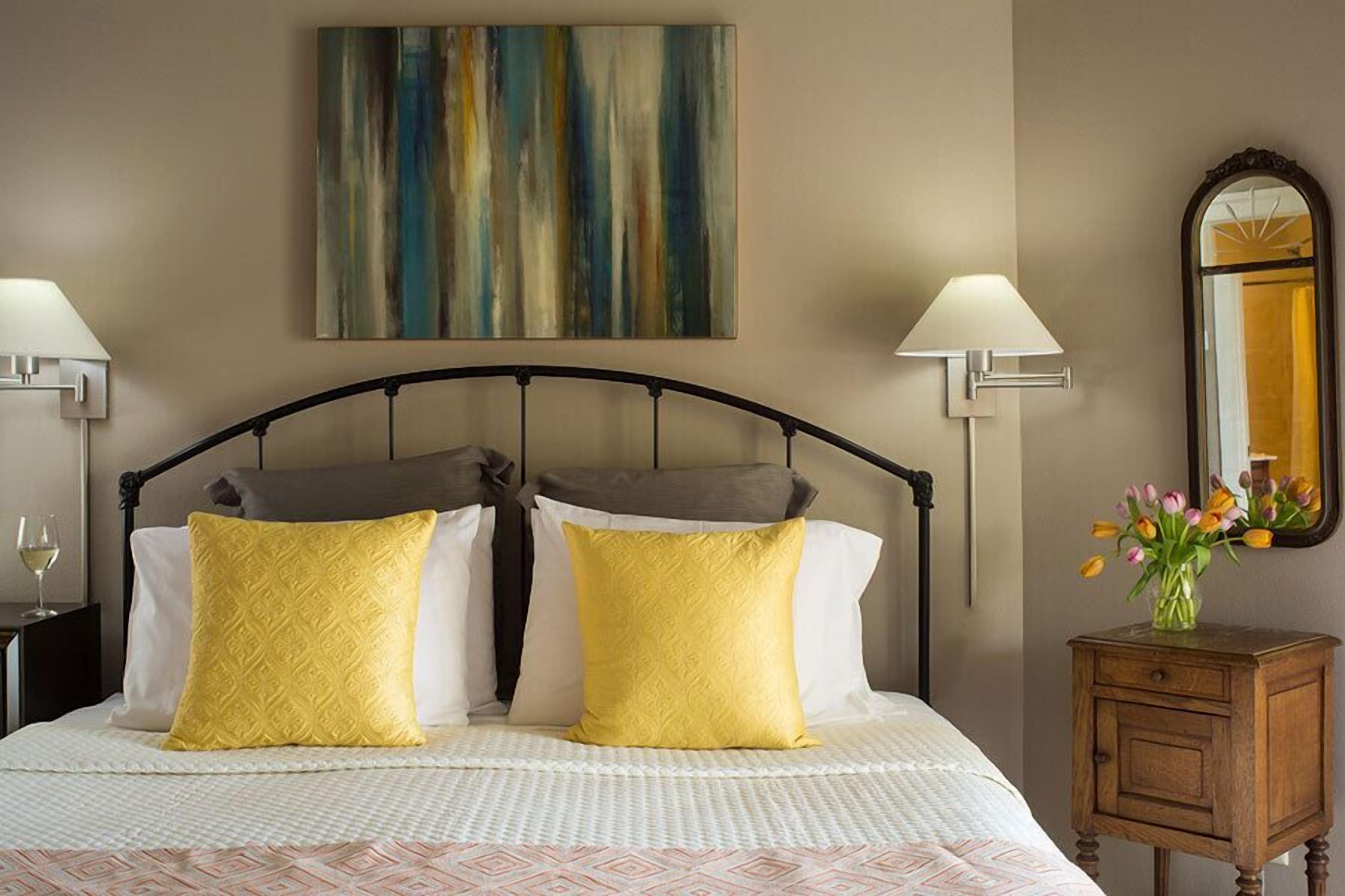 A neatly made bed with two pillows, a bedside table with a lamp, and a mirror on the wall.