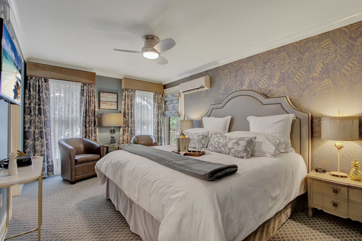 A hotel room with a large bed, a chair, a bedside table, a nightstand, and a ceiling fan.
