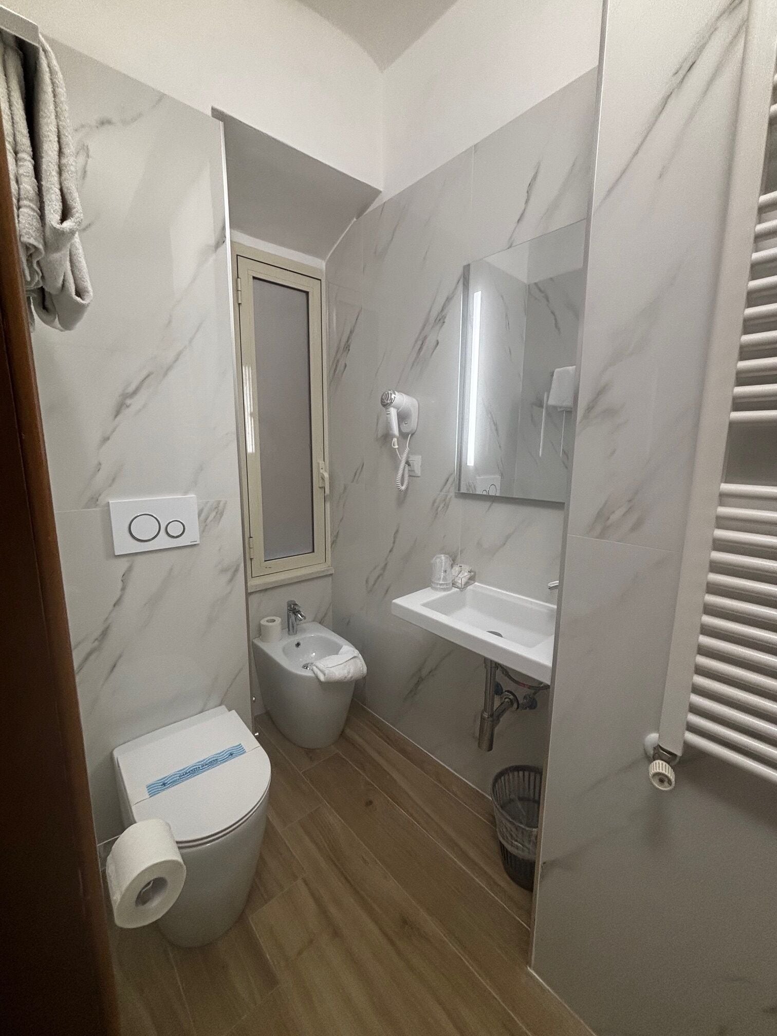 A compact bathroom with a toilet, bidet, sink, and a hairdryer mounted on the wall.