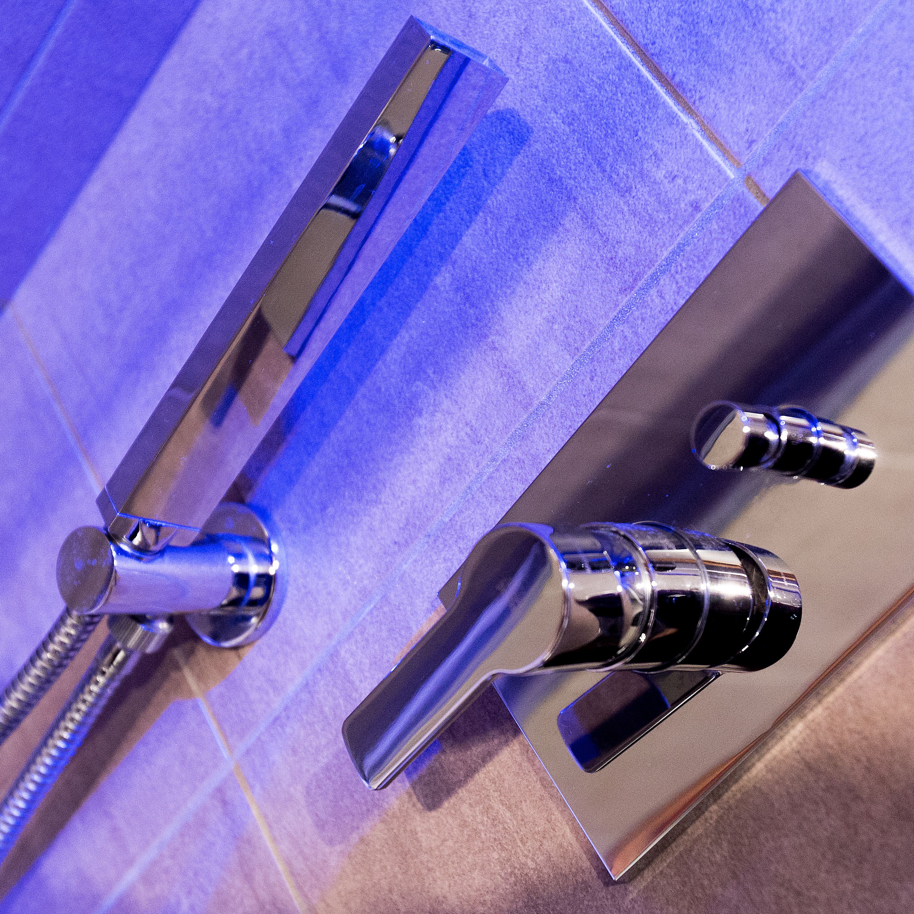 Een badkamer met een modern ontwerp, voorzien van een chromen kraan, een handdouche en een handdoekhouder.