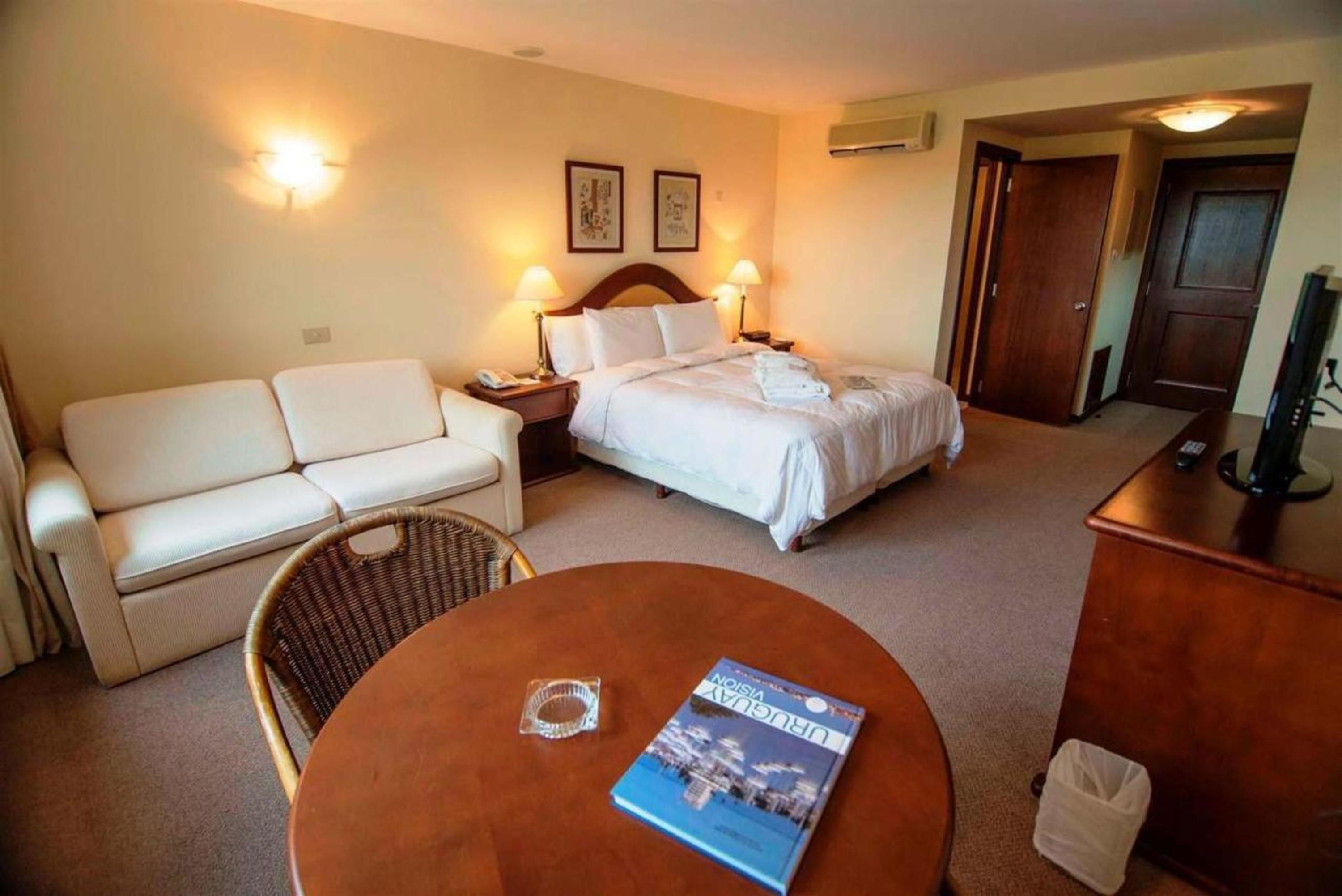 Una habitación de hotel con cama, sofá, mesa de comedor y televisor.