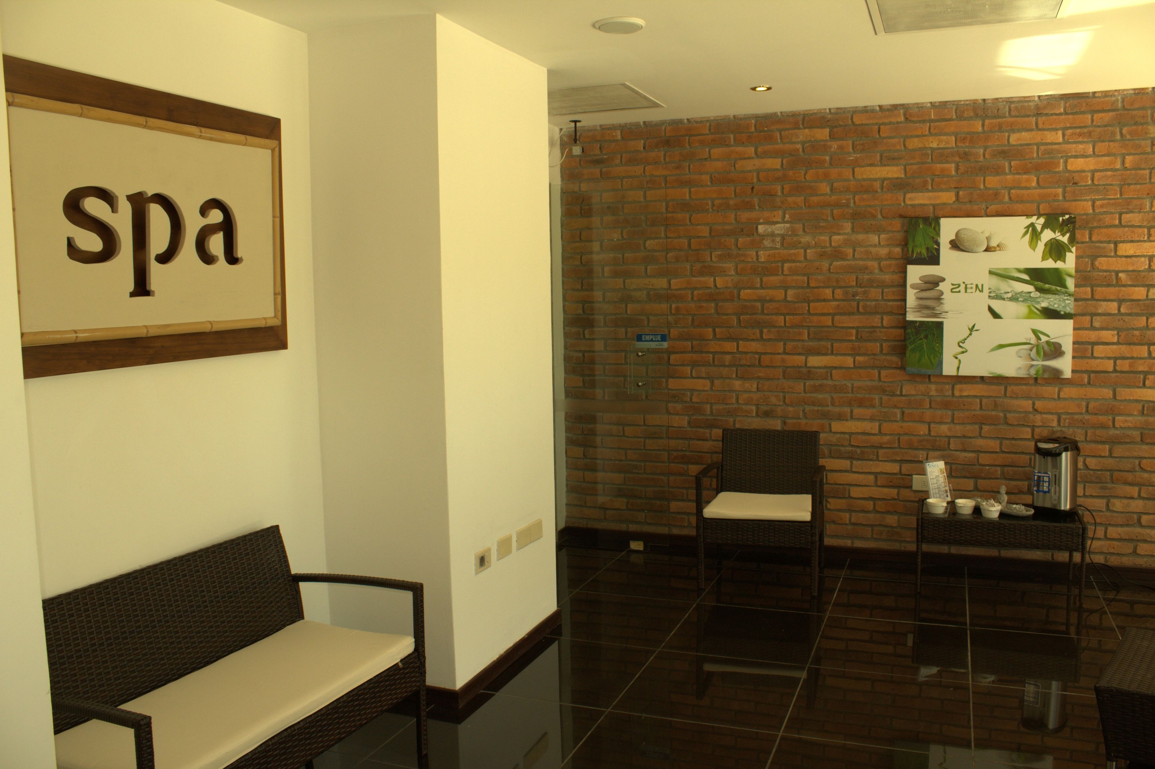 Zona de recepción de spa con un banco, una silla, una máquina de café y una pared con un cartel de 'spa' y una fotografía enmarcada.