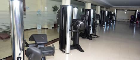 Un gimnasio con diferentes máquinas de ejercicio, un muro de vidrio y piso de baldosas.