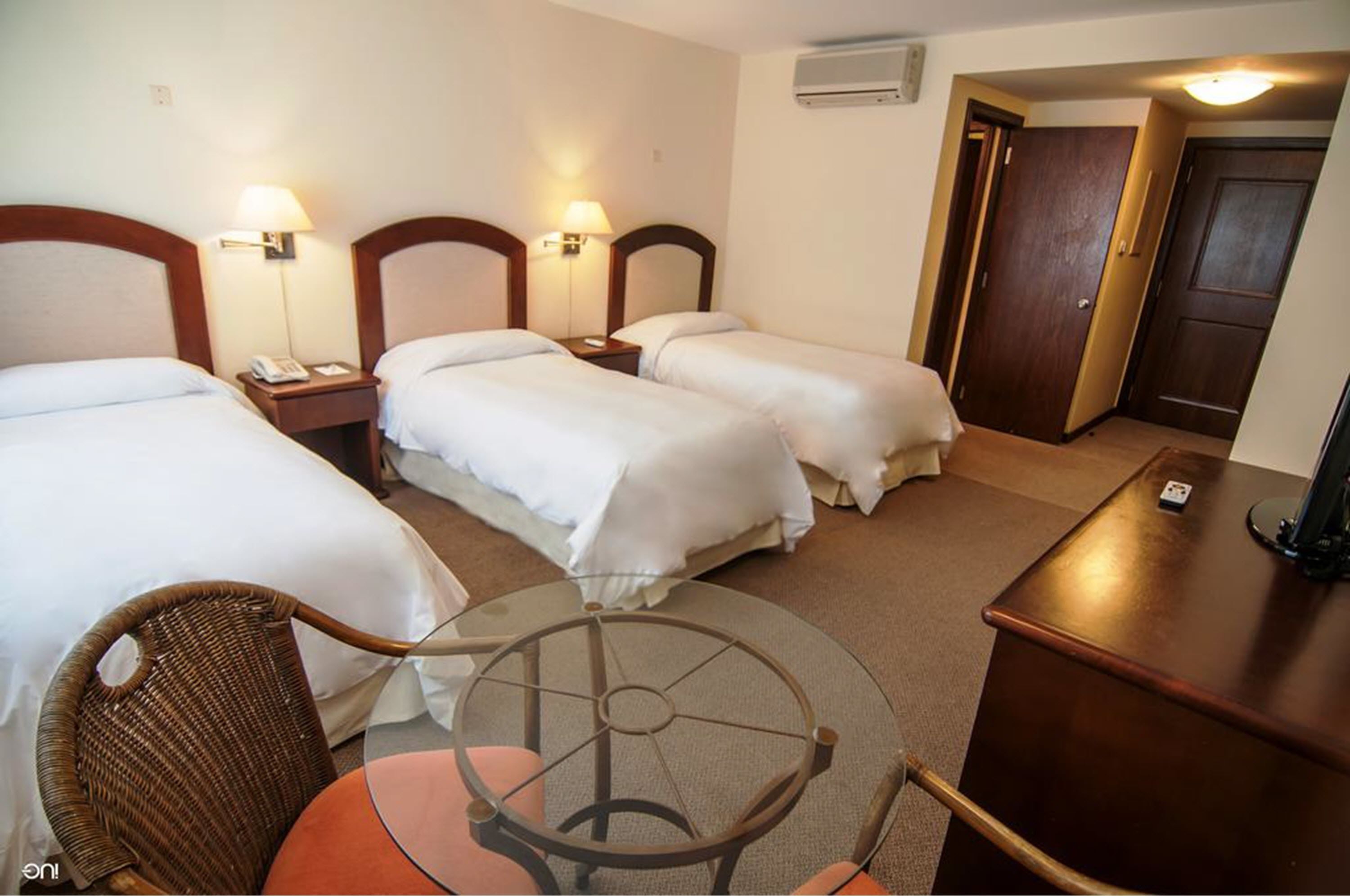 A hotel room with two single beds, a small round table with chairs, a desk, and a chair.