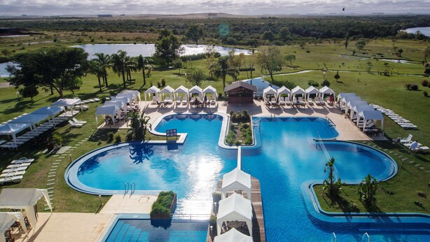 A large, oval-shaped swimming pool with multiple sections and a surrounding deck area with lounge chairs and umbrellas. - Arapey Thermal Resort & Spa (Termas del Arapey)