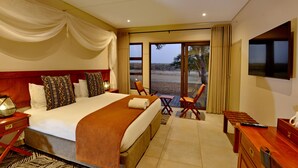 A hotel room with a large bed, a desk, a chair, a TV, and a view of the outdoors. - Hwange Safari Lodge (Dete)