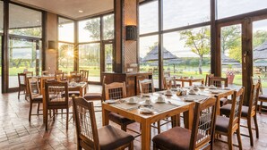 A spacious dining area with large windows, wooden tables, and chairs. - Hwange Safari Lodge (Dete)