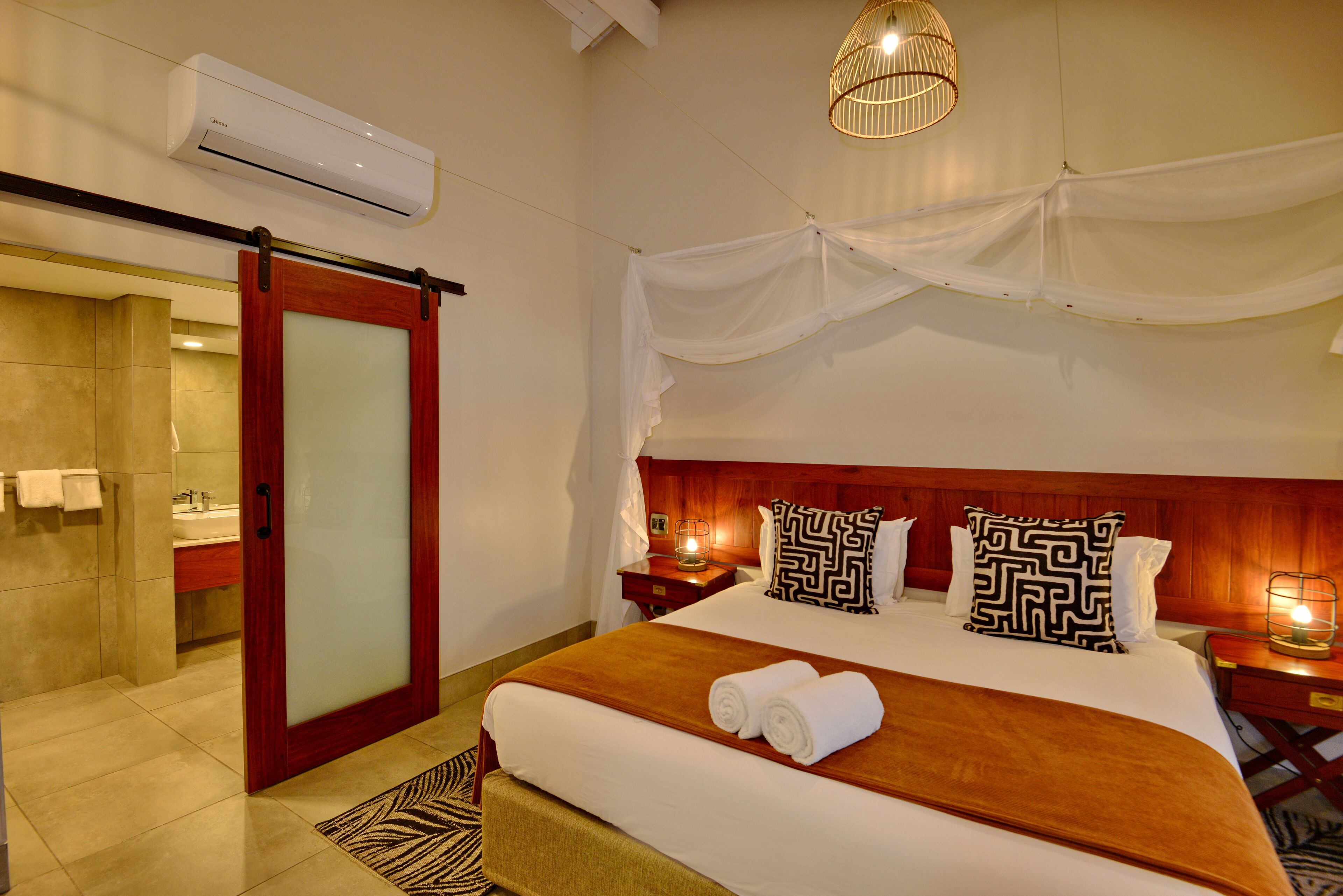 Une chambre d’hôtel comprenant un lit, une table de chevet, une lampe, un miroir, une porte et un appareil de climatisation.
