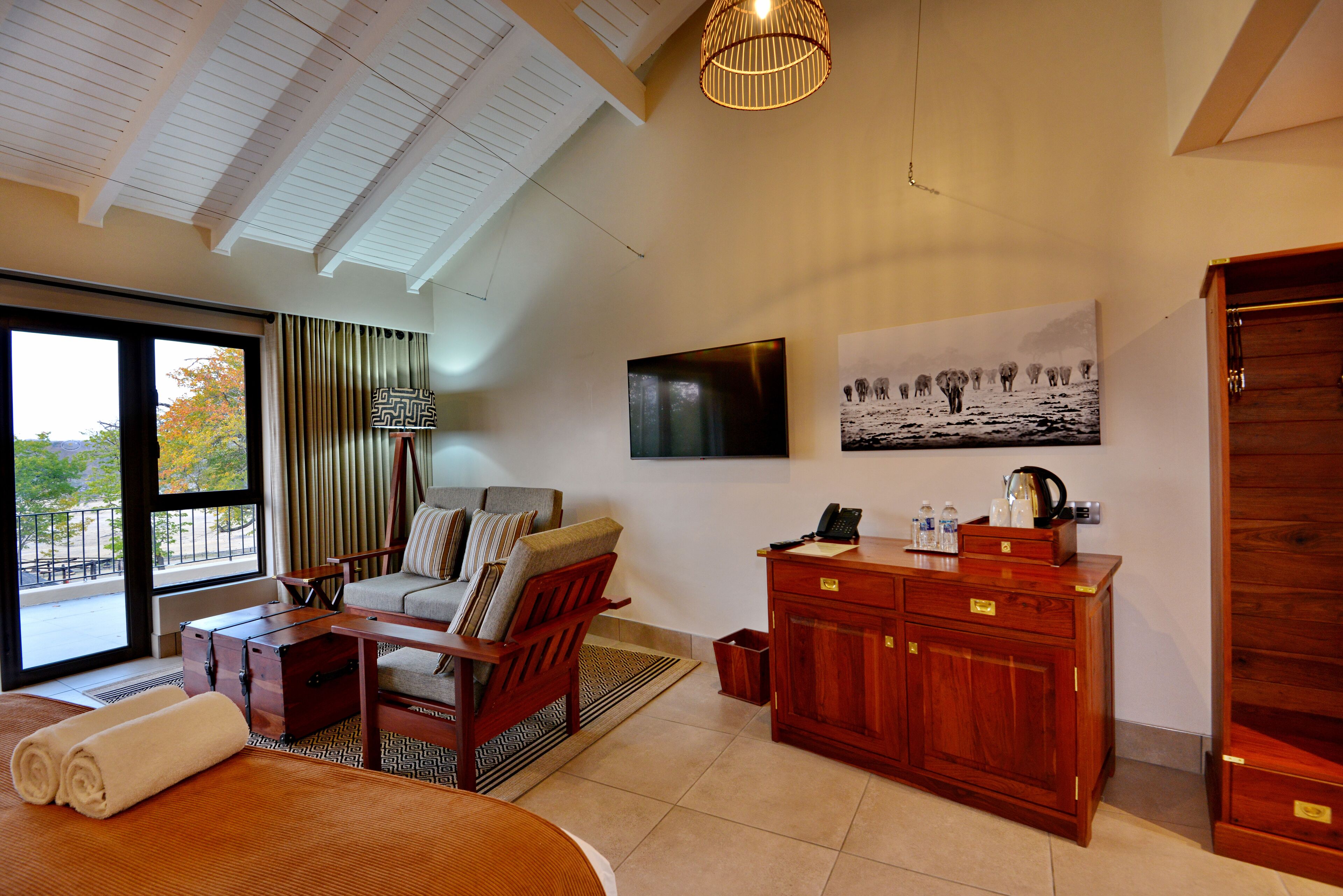 A hotel room with a large bed, a sofa, a wooden cabinet, a television, and a window with curtains.
