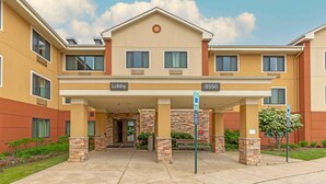 A multi-story hotel with a beige and brown facade, a central entrance with a covered lobby, and a parking sign indicating a parking area. - Extended Stay America Suites Columbia Laurel Ft Meade (Jessup)